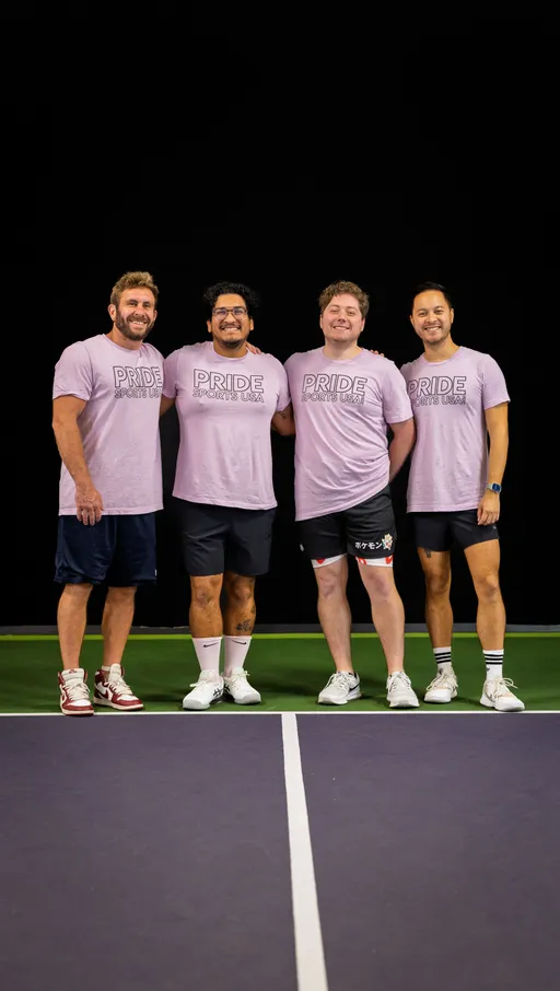 Four pickleball players stand side by side on a court, all wearing matching light purple “Pride Sports USA” t-shirts, athletic shorts, and sneakers, smiling as they pose for a group photo.
