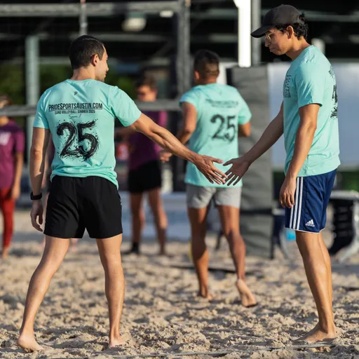 Players wearing matching turquoise shirts and athletic shorts are on a sand volleyball court, giving each other high-fives after a play. The scene is set outdoors with a volleyball net in the background, and the group appears to be celebrating or encouraging one another.